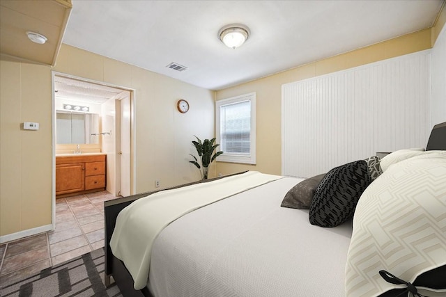 bedroom with light tile patterned floors, visible vents, and ensuite bath