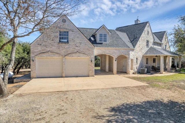 french provincial home featuring a garage, a chimney, central AC unit, and driveway