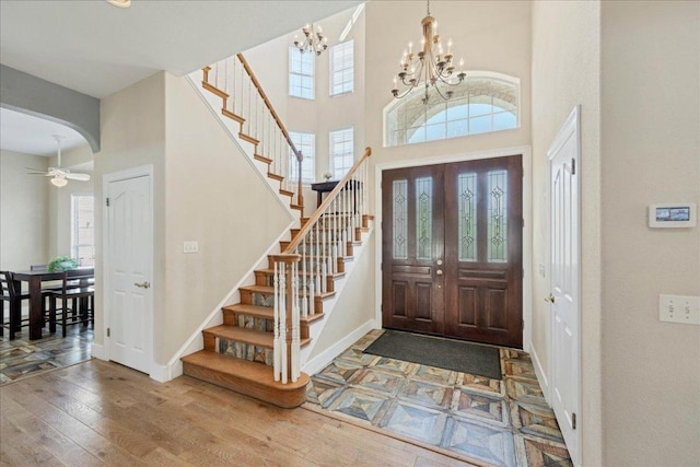 entryway with a notable chandelier, wood-type flooring, arched walkways, baseboards, and stairs