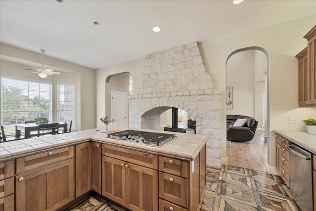 kitchen featuring ceiling fan, tile counters, brown cabinets, arched walkways, and stainless steel appliances