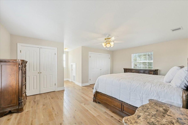 bedroom with light wood-type flooring, visible vents, two closets, baseboards, and ceiling fan