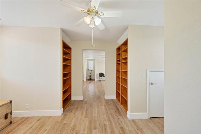 hallway with light wood-style flooring, built in shelves, and baseboards