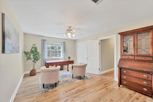 living area featuring a ceiling fan, baseboards, light wood finished floors, and a textured ceiling