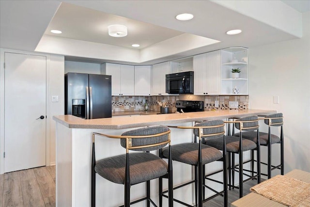 kitchen featuring a tray ceiling, black appliances, a peninsula, and decorative backsplash