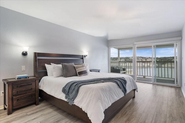 bedroom with wood finished floors, a water view, and access to outside