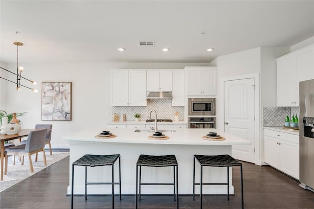 kitchen featuring visible vents, under cabinet range hood, a breakfast bar area, light countertops, and stainless steel appliances