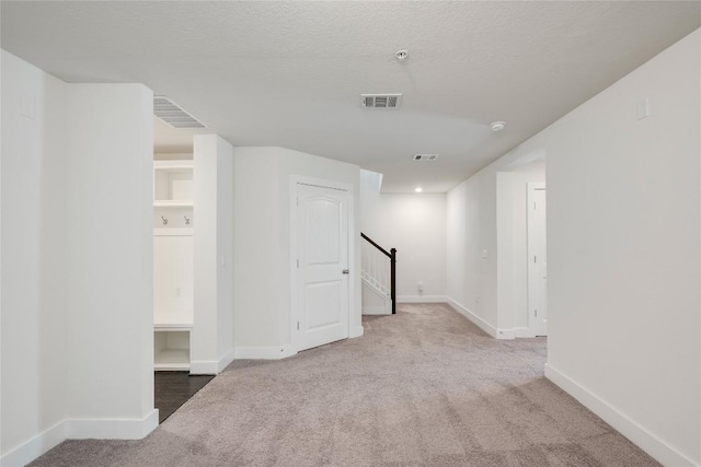 basement featuring a textured ceiling, carpet, visible vents, and baseboards