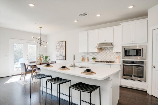 kitchen featuring tasteful backsplash, visible vents, under cabinet range hood, stainless steel appliances, and a sink