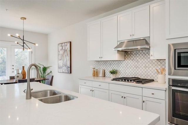 kitchen with under cabinet range hood, light countertops, decorative backsplash, stainless steel appliances, and a sink