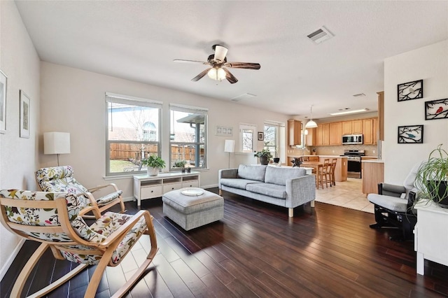 living area featuring ceiling fan, wood finished floors, visible vents, and a healthy amount of sunlight