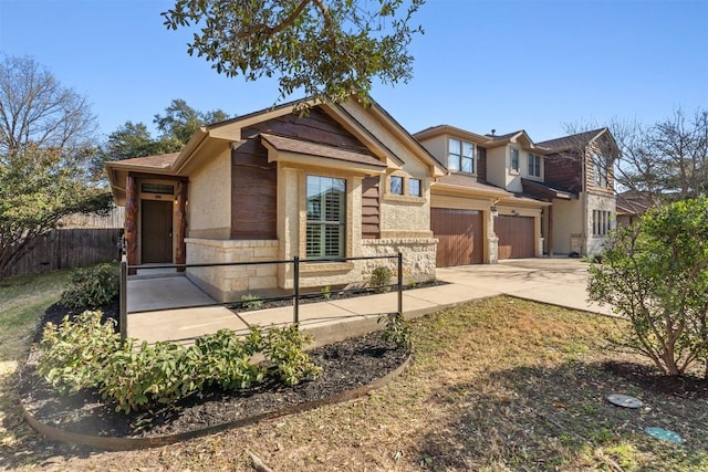 view of front of house featuring stone siding, an attached garage, driveway, and fence