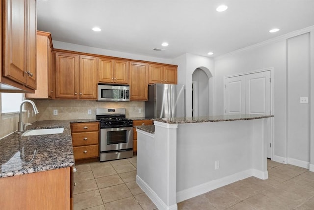 kitchen featuring a sink, dark stone counters, appliances with stainless steel finishes, and a center island