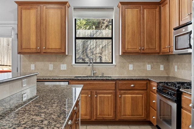 kitchen with a sink, dark stone counters, brown cabinets, and stainless steel appliances