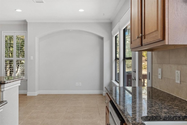 kitchen featuring dark stone countertops, baseboards, tasteful backsplash, and ornamental molding