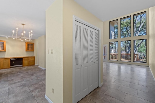 corridor featuring a chandelier, light tile patterned floors, and baseboards