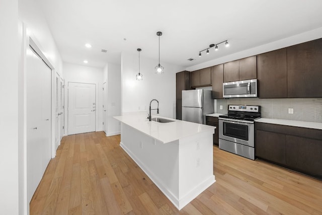 kitchen with a sink, stainless steel appliances, dark brown cabinets, and light wood finished floors