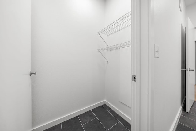 laundry area with dark tile patterned flooring and baseboards