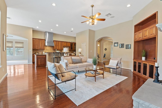 living room with arched walkways, visible vents, a ceiling fan, and dark wood-style floors