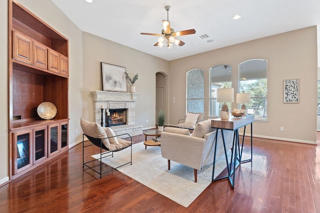 living room featuring dark wood-style floors, baseboards, visible vents, a fireplace, and ceiling fan