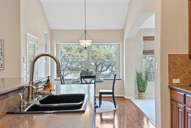 kitchen with decorative light fixtures, vaulted ceiling, wood finished floors, arched walkways, and a sink