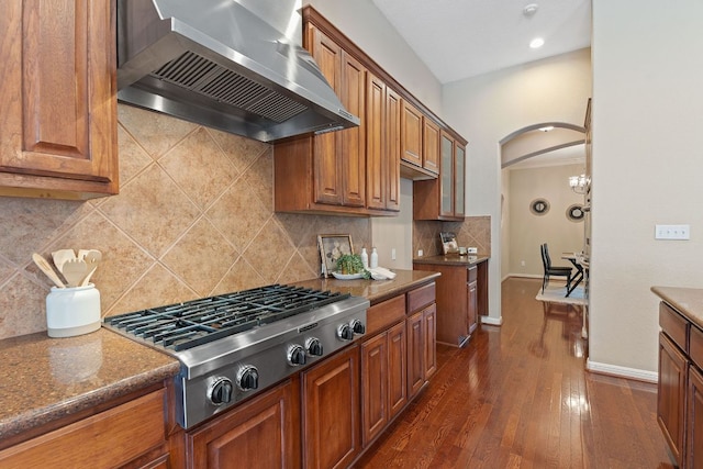 kitchen with stainless steel gas cooktop, brown cabinets, wall chimney exhaust hood, and dark wood-type flooring