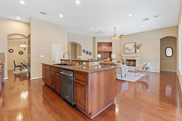 kitchen with a sink, arched walkways, a fireplace, brown cabinetry, and dishwasher