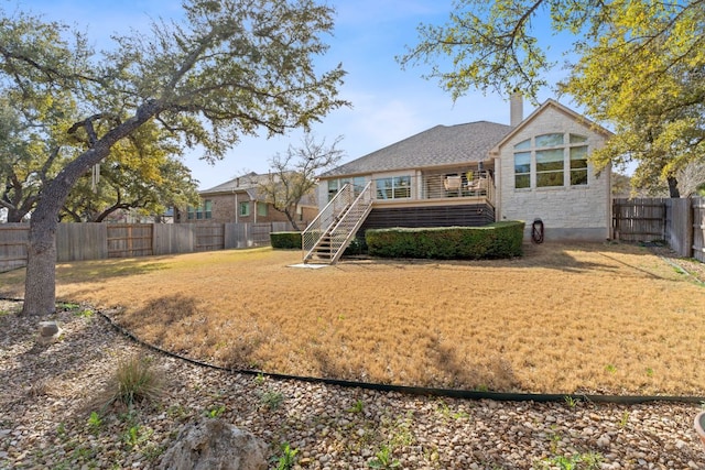 rear view of house with a wooden deck, a yard, a fenced backyard, a chimney, and stairs