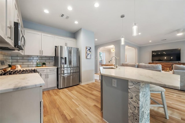 kitchen with arched walkways, a sink, stainless steel appliances, open floor plan, and backsplash