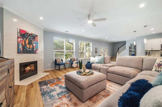 living area with a high end fireplace, crown molding, ceiling fan, stairway, and light wood-style flooring