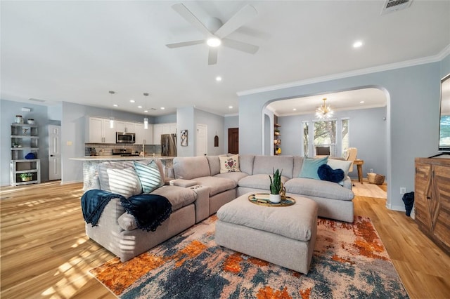 living room featuring light wood-type flooring, visible vents, arched walkways, and ceiling fan with notable chandelier