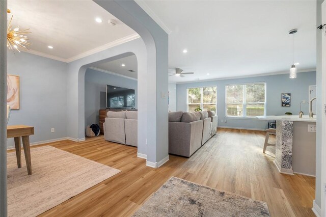 living room with arched walkways, light wood-style flooring, a ceiling fan, and baseboards