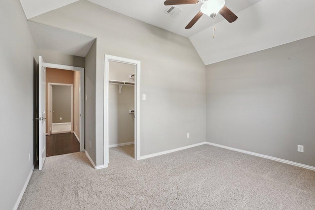 unfurnished bedroom with a spacious closet, visible vents, baseboards, lofted ceiling, and carpet floors