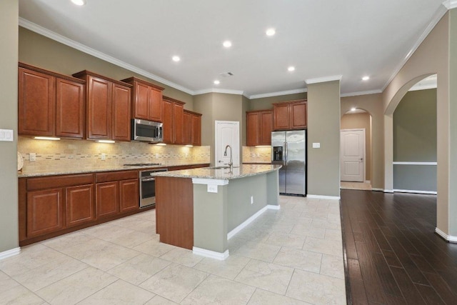 kitchen with light stone countertops, an island with sink, appliances with stainless steel finishes, arched walkways, and a sink