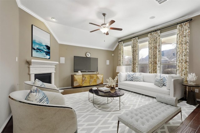 living area with wood finished floors, lofted ceiling, a fireplace, ceiling fan, and crown molding