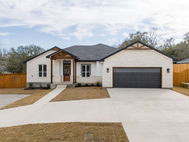 view of front of property with fence, driveway, an attached garage, a shingled roof, and stone siding