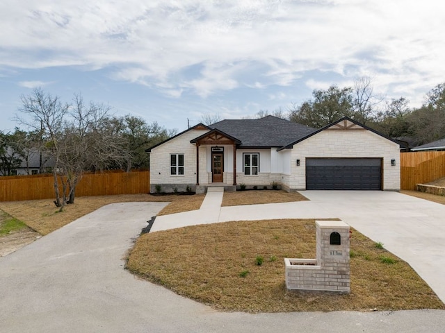 view of front facade featuring driveway, stone siding, fence, an attached garage, and a shingled roof