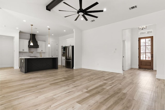 unfurnished living room featuring beamed ceiling, ceiling fan with notable chandelier, visible vents, and light wood-type flooring