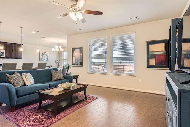 living area with visible vents, baseboards, wood finished floors, and ceiling fan with notable chandelier