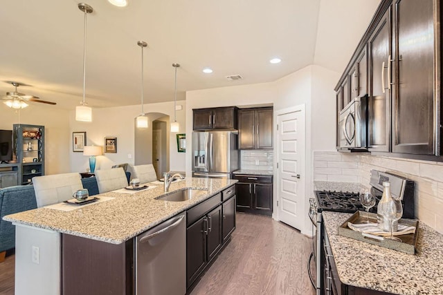 kitchen with dark brown cabinetry, open floor plan, appliances with stainless steel finishes, arched walkways, and a sink