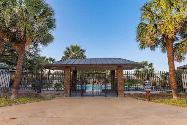 view of community featuring a swimming pool, concrete driveway, and fence