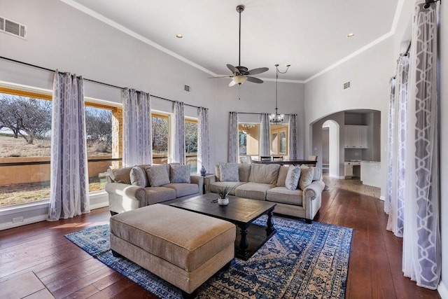 living room with visible vents, ceiling fan with notable chandelier, arched walkways, and dark wood-style flooring