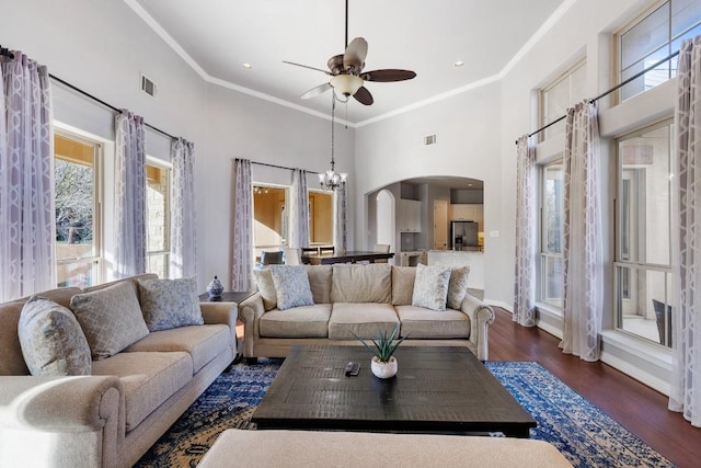 living room featuring arched walkways, wood finished floors, crown molding, and ceiling fan with notable chandelier