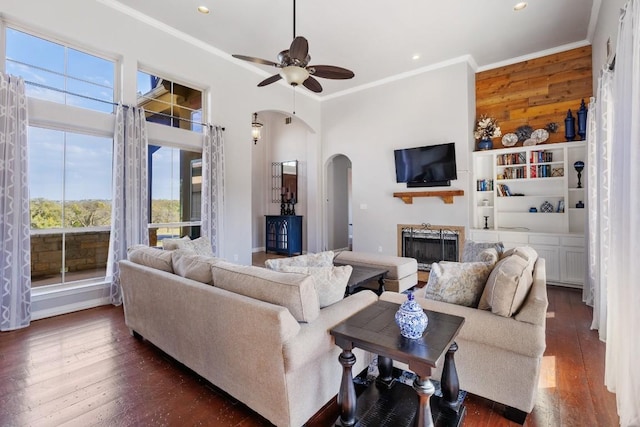 living area with a fireplace, arched walkways, dark wood-style flooring, ceiling fan, and crown molding