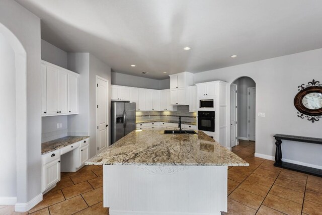 kitchen with a sink, backsplash, white cabinetry, stainless steel appliances, and arched walkways