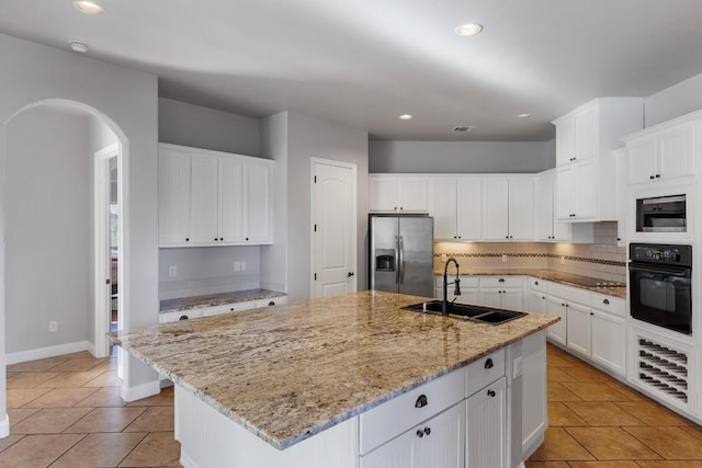 kitchen with a kitchen island with sink, a sink, decorative backsplash, black oven, and stainless steel fridge