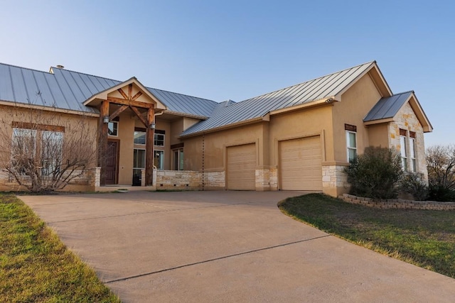 view of front of home with driveway, a standing seam roof, stone siding, an attached garage, and metal roof