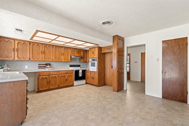 kitchen featuring oven, electric range, brown cabinets, visible vents, and a sink