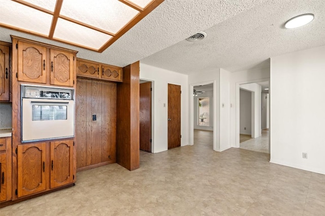 kitchen with white oven, brown cabinets, light floors, and visible vents