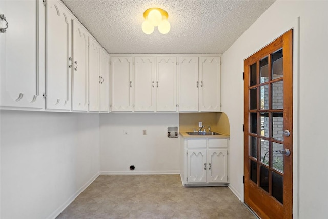 washroom with a sink, a textured ceiling, cabinet space, baseboards, and hookup for a washing machine