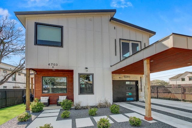 rear view of house featuring board and batten siding, driveway, and fence